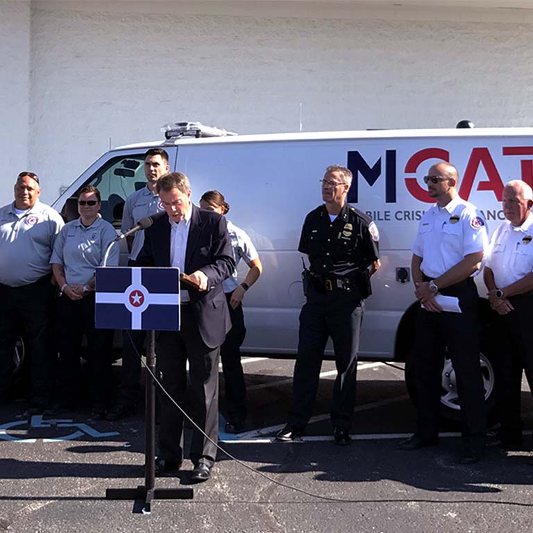 Indianapolis Mayor Joe Hogsett speaks while public safety workers stand by an MCAT van.