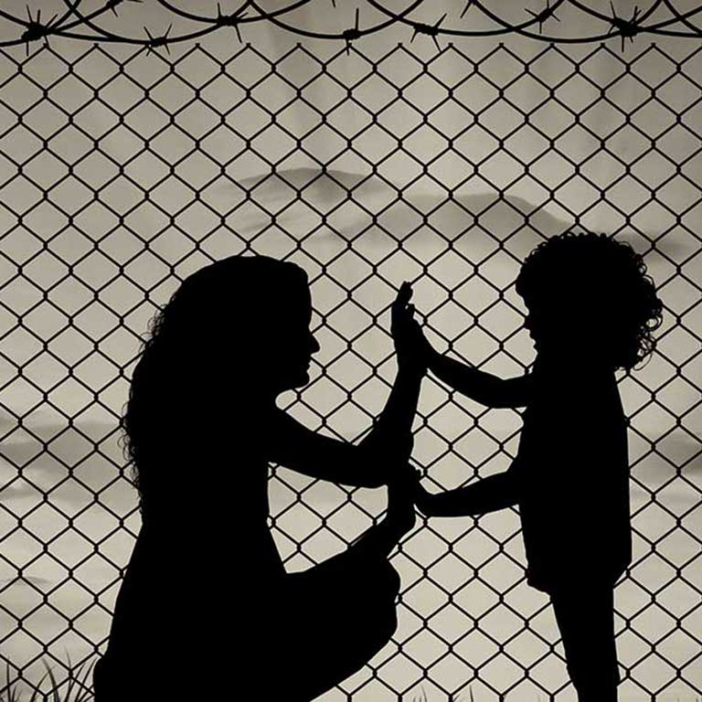 Mom and child touching hands behind barbed fence.